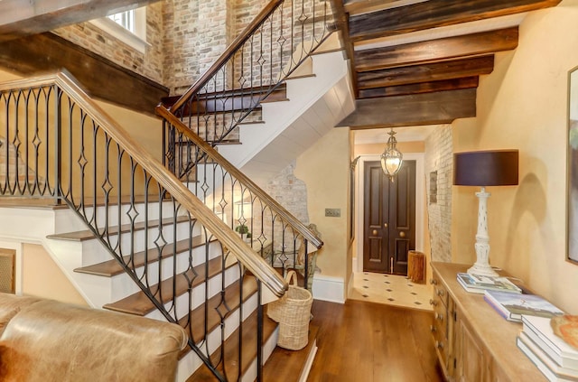 stairs featuring hardwood / wood-style flooring, a high ceiling, and beam ceiling