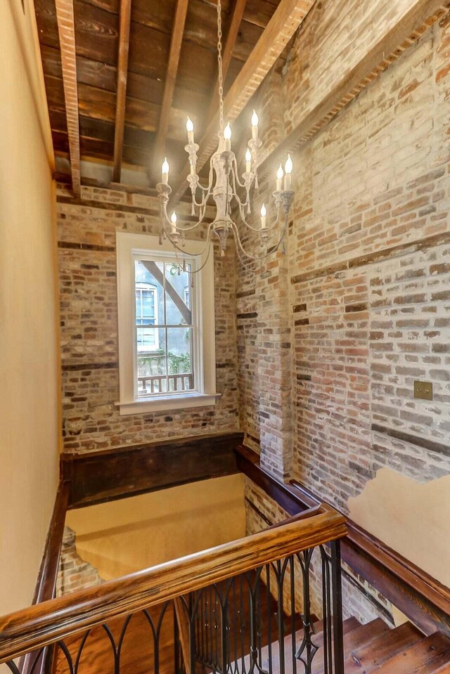 staircase with wood ceiling, brick wall, beam ceiling, and a chandelier