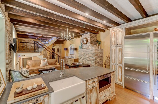 kitchen featuring beamed ceiling, sink, built in fridge, and light wood-type flooring
