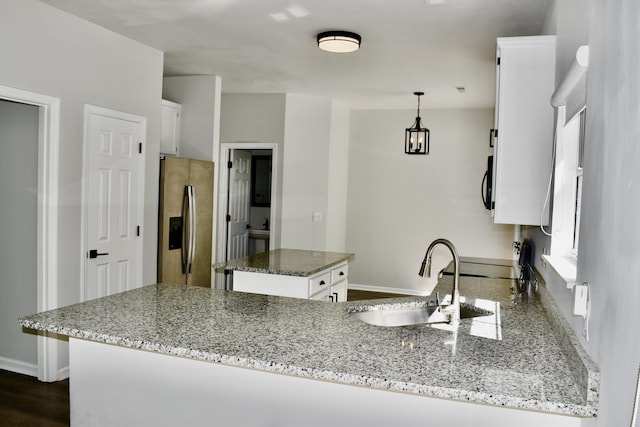kitchen with light stone counters, a sink, stainless steel fridge with ice dispenser, white cabinetry, and baseboards