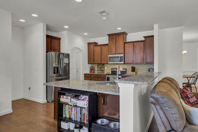 kitchen with dark hardwood / wood-style floors, appliances with stainless steel finishes, light stone counters, kitchen peninsula, and a breakfast bar area