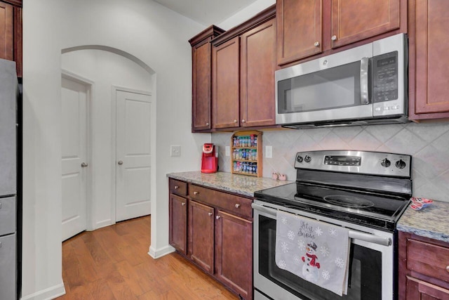 kitchen with tasteful backsplash, light stone countertops, appliances with stainless steel finishes, and light hardwood / wood-style flooring