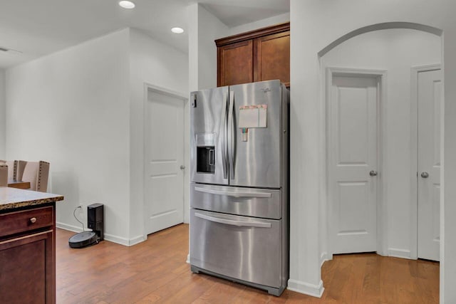 kitchen with stainless steel fridge with ice dispenser, light stone countertops, and light wood-type flooring