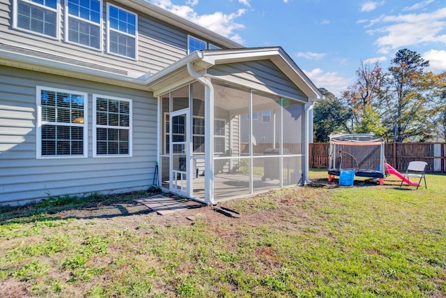 rear view of property featuring a lawn, a sunroom, a trampoline, and a patio