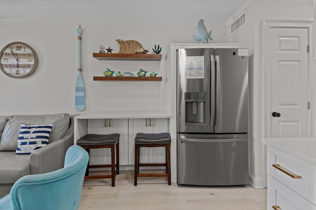 kitchen with visible vents, light wood-style flooring, a breakfast bar area, crown molding, and stainless steel refrigerator with ice dispenser