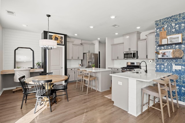 kitchen with a center island, sink, stainless steel appliances, decorative light fixtures, and a breakfast bar