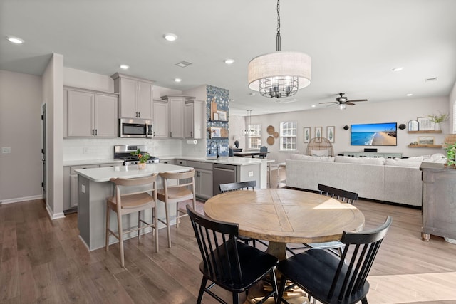 dining space with ceiling fan with notable chandelier, light wood-type flooring, and sink