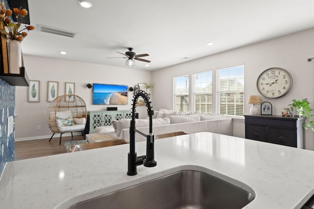 kitchen featuring hardwood / wood-style flooring, ceiling fan, light stone counters, and sink