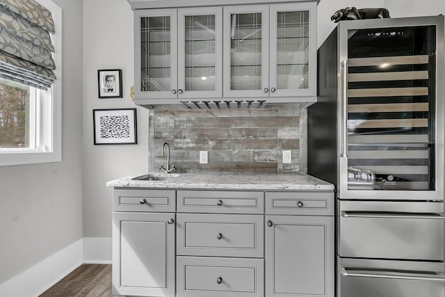 kitchen with dark wood finished floors, wine cooler, a sink, light stone countertops, and backsplash