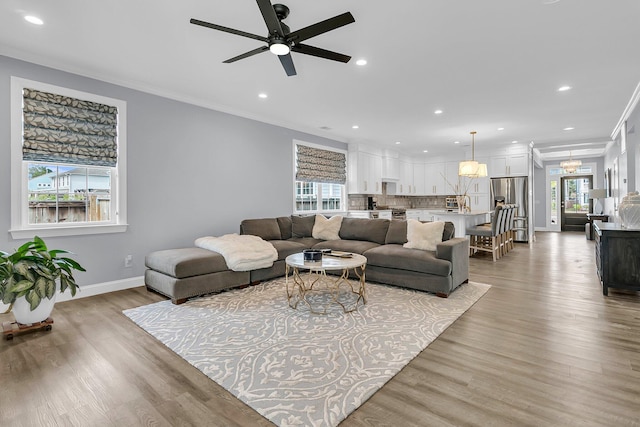 living area with baseboards, ornamental molding, recessed lighting, and light wood-style floors