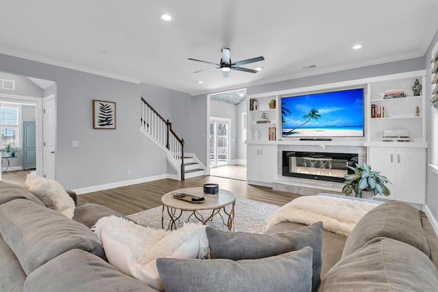 living area featuring built in features, light wood-style floors, stairway, and a tiled fireplace