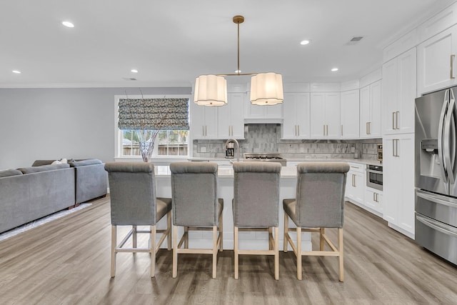 kitchen with appliances with stainless steel finishes, light countertops, a kitchen bar, and tasteful backsplash