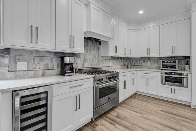 kitchen with beverage cooler, stainless steel appliances, light wood-style flooring, and white cabinets