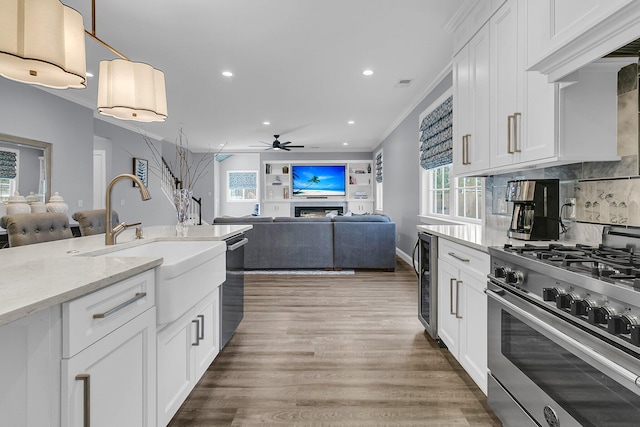 kitchen with a warm lit fireplace, a sink, high end stainless steel range, light wood finished floors, and crown molding