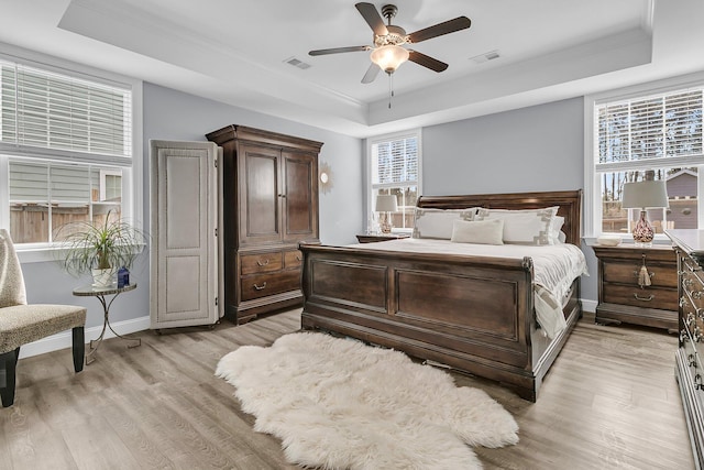 bedroom with light wood-style floors, multiple windows, visible vents, and a raised ceiling