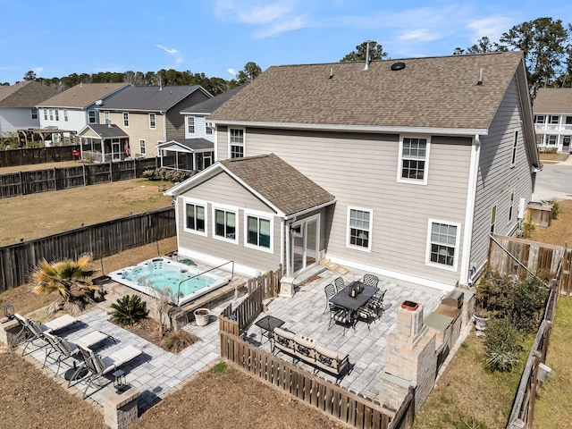 rear view of property with outdoor dining area, a shingled roof, an outdoor hot tub, a patio area, and a fenced backyard