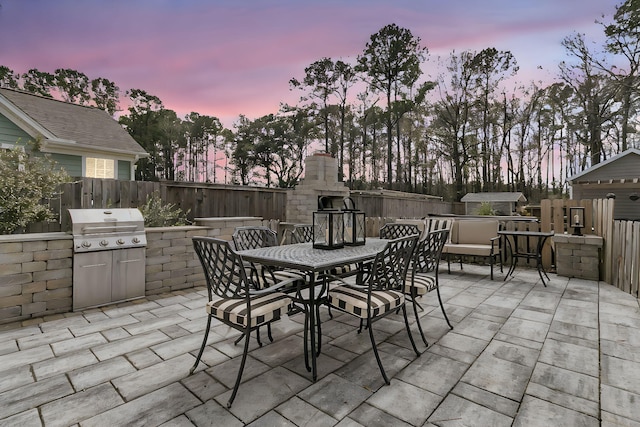 view of patio with outdoor dining area, an outdoor kitchen, area for grilling, a fireplace, and fence