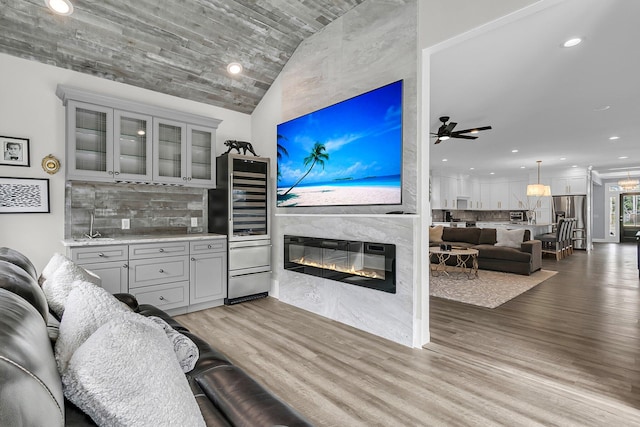 living room featuring a glass covered fireplace, lofted ceiling, wine cooler, wood finished floors, and recessed lighting