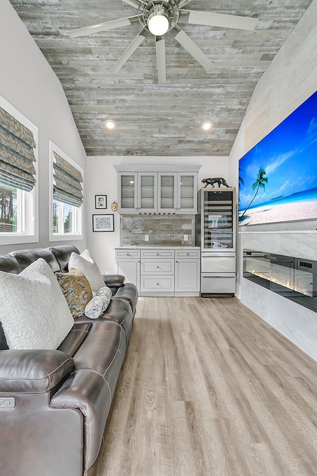 living room with ceiling fan, light wood-style flooring, vaulted ceiling, and a glass covered fireplace