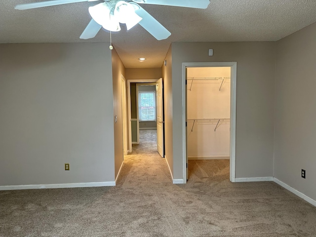 unfurnished bedroom featuring light colored carpet, a spacious closet, baseboards, and a textured ceiling