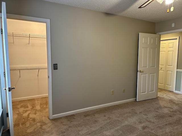 unfurnished bedroom featuring a walk in closet, a closet, light colored carpet, and a textured ceiling