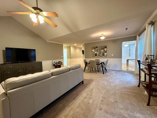 living room with lofted ceiling, visible vents, ornamental molding, a ceiling fan, and light carpet