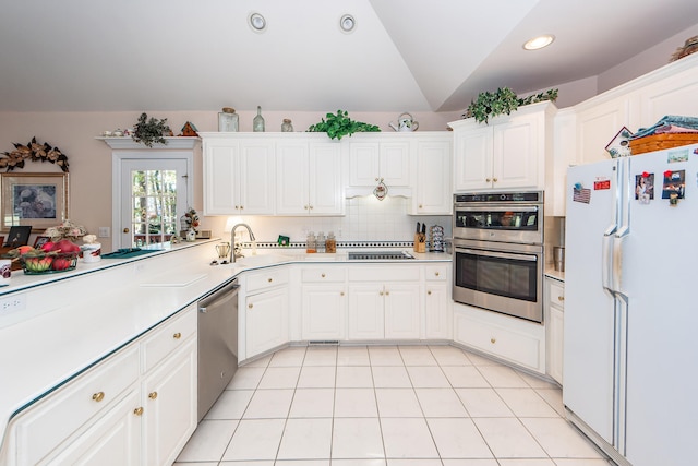 kitchen featuring stainless steel appliances, vaulted ceiling, light tile patterned flooring, white cabinets, and tasteful backsplash