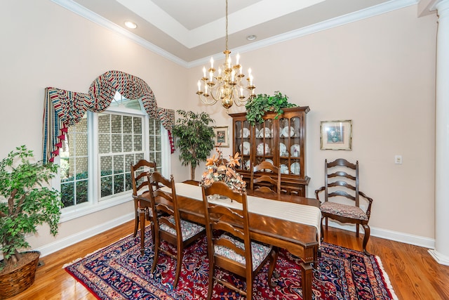 dining space with ornamental molding, a notable chandelier, hardwood / wood-style flooring, and a tray ceiling