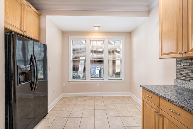 kitchen featuring light tile patterned floors, dark stone countertops, black refrigerator with ice dispenser, crown molding, and baseboards