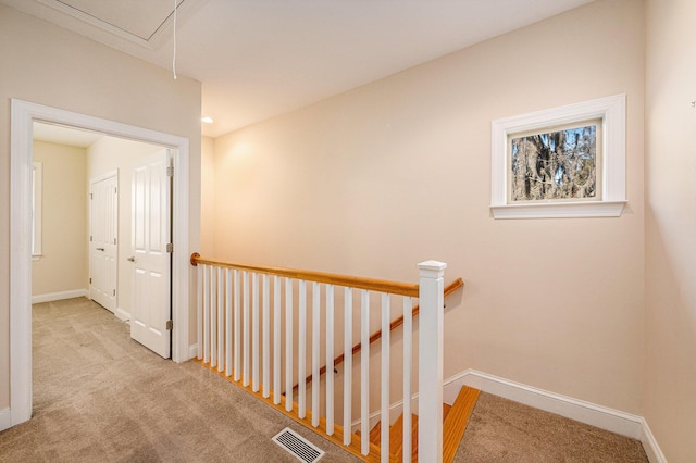 corridor featuring attic access, an upstairs landing, visible vents, and carpet flooring