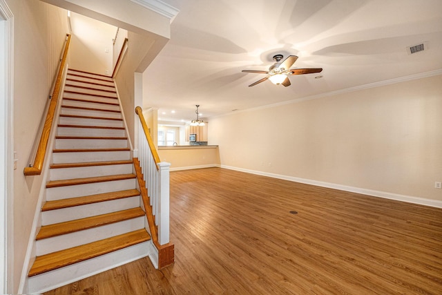 stairs with visible vents, ornamental molding, ceiling fan with notable chandelier, and wood finished floors