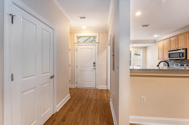 corridor with ornamental molding, visible vents, light wood-style flooring, and baseboards