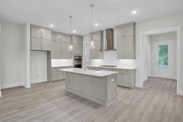 3029 Robeson Trce, Johns Island, SC 29455 - kitchen featuring wall chimney range hood, appliances with stainless steel finishes, light countertops, light wood-style floors, and a center island with sink