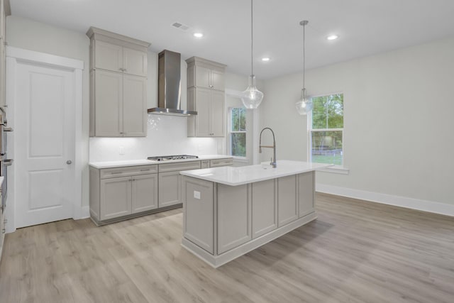 3029 Robeson Trce, Johns Island, SC 29455 - kitchen with wall chimney range hood, stainless steel gas cooktop, light wood finished floors, light countertops, and a center island with sink