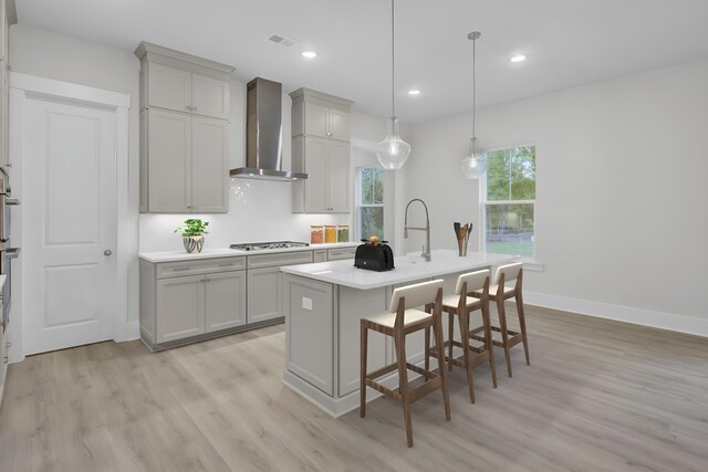 3029 Robeson Trce, Johns Island, SC 29455 - kitchen with wall chimney exhaust hood, stainless steel gas stovetop, light wood-style flooring, a kitchen island with sink, and a kitchen breakfast bar