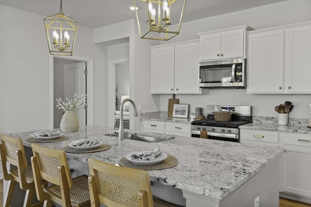 kitchen featuring stainless steel appliances, white cabinetry, a sink, and an inviting chandelier