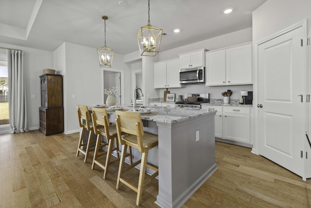 kitchen with light wood finished floors, stainless steel microwave, stove, a kitchen island with sink, and white cabinetry