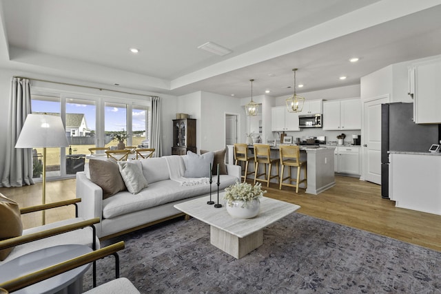 living area featuring a notable chandelier, a tray ceiling, recessed lighting, and light wood-style floors