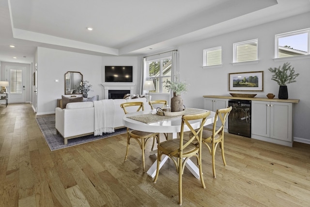 dining space with light wood finished floors, a raised ceiling, wine cooler, a fireplace, and recessed lighting