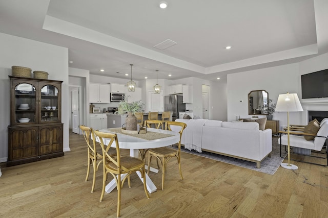 dining space featuring light wood-style floors, a fireplace, a raised ceiling, and recessed lighting