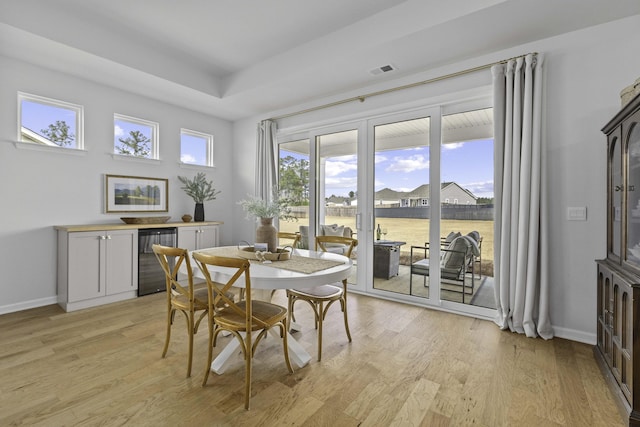 dining area with wine cooler, light wood-type flooring, visible vents, and baseboards