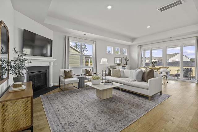 living room with a fireplace with flush hearth, light wood-type flooring, a healthy amount of sunlight, and visible vents