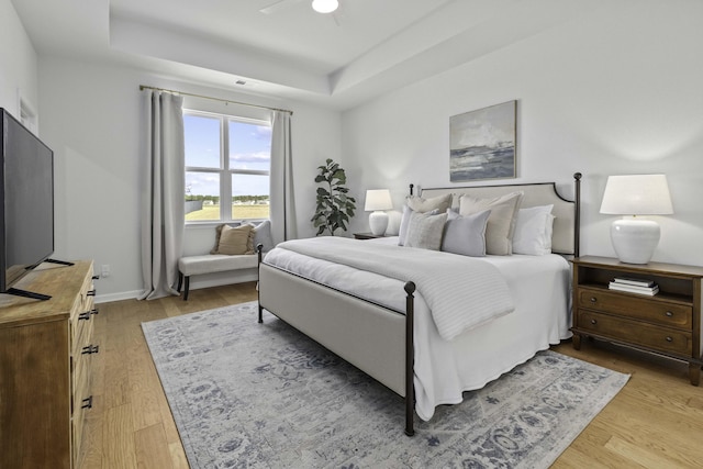 bedroom featuring light wood finished floors, a raised ceiling, visible vents, ceiling fan, and baseboards