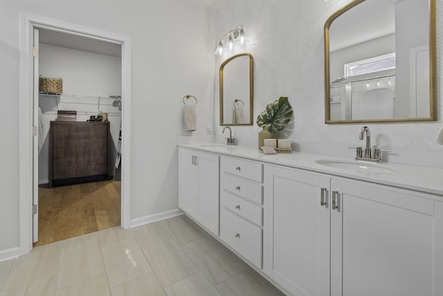 bathroom with double vanity, wallpapered walls, baseboards, and a sink