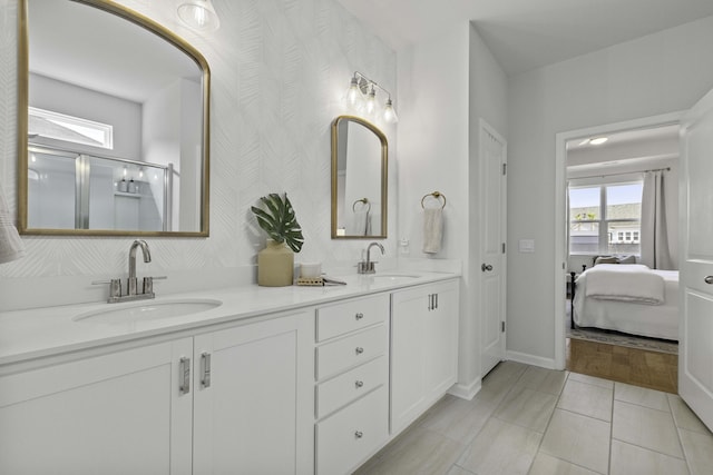 ensuite bathroom with baseboards, double vanity, a sink, and wallpapered walls