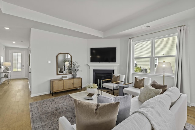 living room featuring light wood-style flooring, recessed lighting, visible vents, baseboards, and a glass covered fireplace