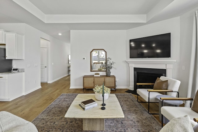 living area with a tray ceiling, baseboards, wood finished floors, and a glass covered fireplace