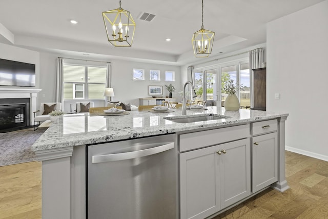 kitchen with a raised ceiling, hanging light fixtures, open floor plan, a sink, and dishwasher