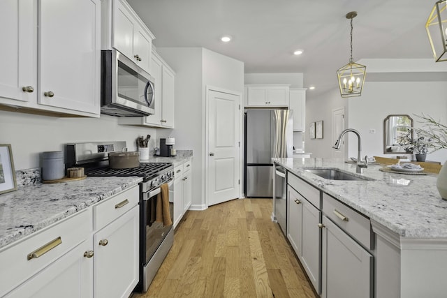 kitchen with a kitchen island with sink, a sink, white cabinets, light wood-style floors, and appliances with stainless steel finishes