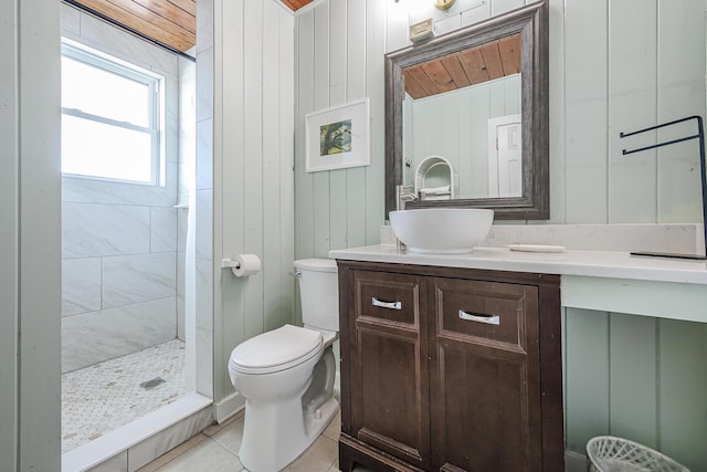 bathroom featuring vanity, wood walls, tile patterned flooring, toilet, and tiled shower